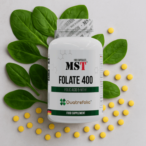 MST® Folate 400 (Quatrefolic®) 180 капсул на світло-сірому фоні серед зеленого шпинату та жовтих таблеток — символ природного джерела фолатів, енергії та жіночого здоров’я.