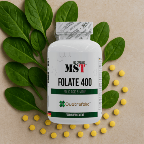 Банка MST® Folate 400 (Quatrefolic®) 180 капсул на бежевому фоні серед листя шпинату та жовтих таблеток — асоціація з натуральністю, чистотою та підтримкою жіночого організму.